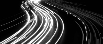 Long-exposure photo of a highway at night, with curved streaks of white and red lights from moving vehicles, capturing the fast-paced energy of enterprise and ai-driven innovation against a dark background.