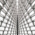 A symmetrical view of a modern enterprise building’s interior ceiling featuring repeating horizontal slats and large windows, creating a geometric, tunnel-like perspective.