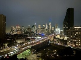 Nighttime view of Manhattan skyline with illuminated skyscrapers, including enterprise buildings, Brooklyn Bridge, and busy traffic heading into the city.