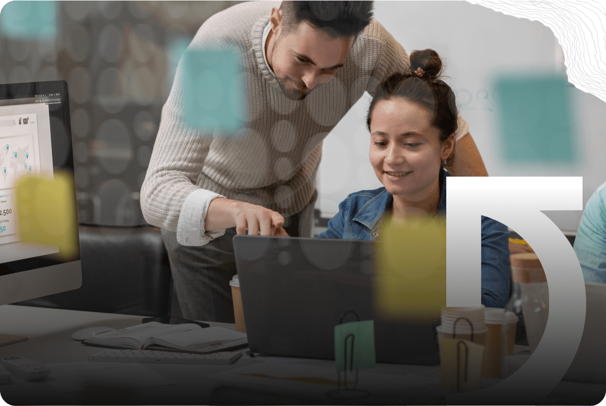 A man and woman work together at a desk with a laptop; the man points at the screen while the woman smiles, sharing success stories. Sticky notes and office supplies are visible.