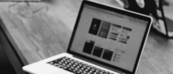 A laptop displaying an AI-powered website design interface sits on a wooden table, with another laptop partially visible in the background.